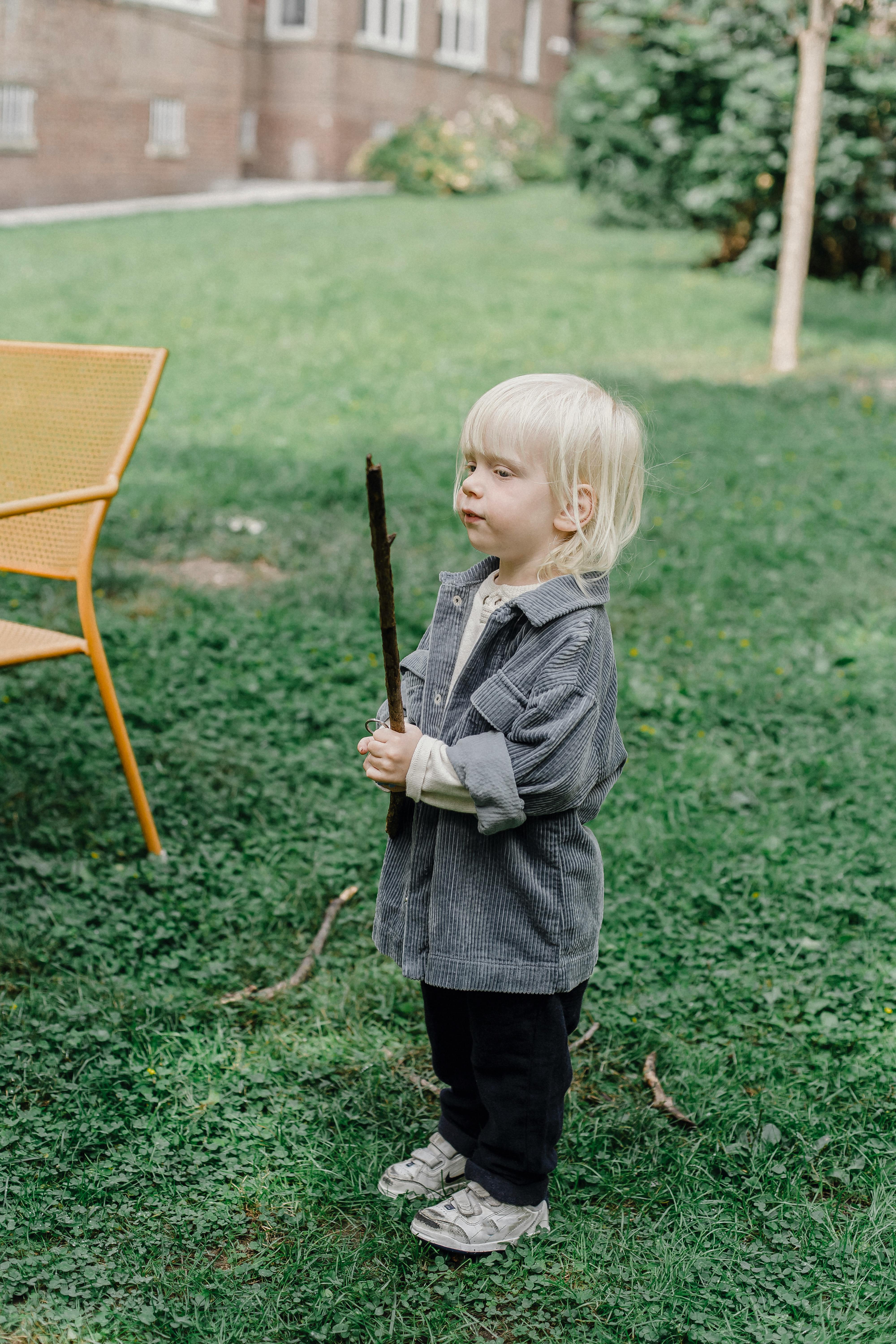 Blond child enjoying playtime with a stick in a green backyard setting.