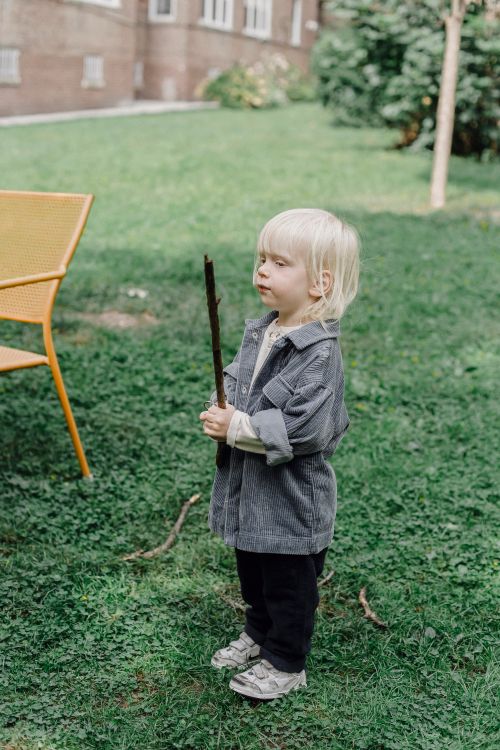 Free Full body side view of cute little kid with blond hair standing with toy on grassy lawn with building and tree on blurred background Stock Photo