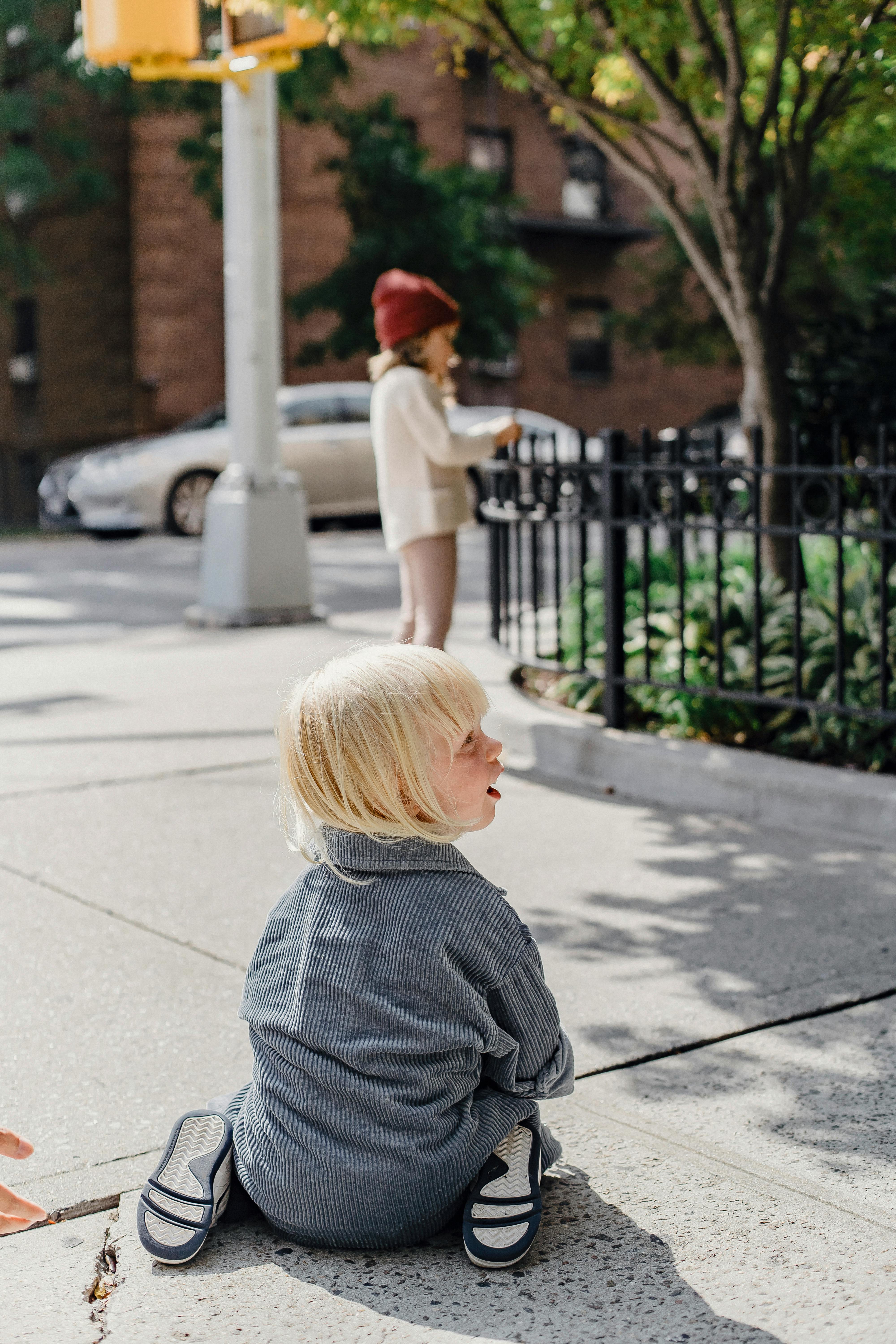 little boy sitting on sidewalk