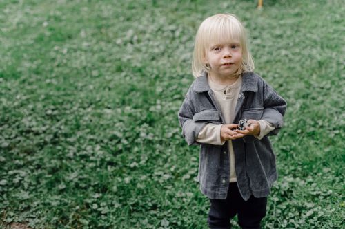 Free From above of cute kid with toy looking at camera while standing on grassy lawn against blurred background on street Stock Photo