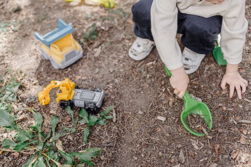 Free High angle of unrecognizable child playing with plastic toys sitting on ground in yard Stock Photo