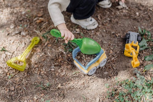 Unrecognizable little child playing with plastic toy car and shovel in calm sunny yard