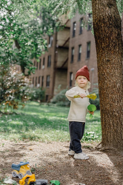 Little kid with toys near big tree in garden