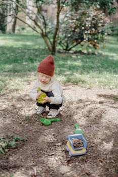 阳光明媚的公园里，一个戴着无檐帽的小孩正玩着玩具卡车，沉浸在玩耍中
