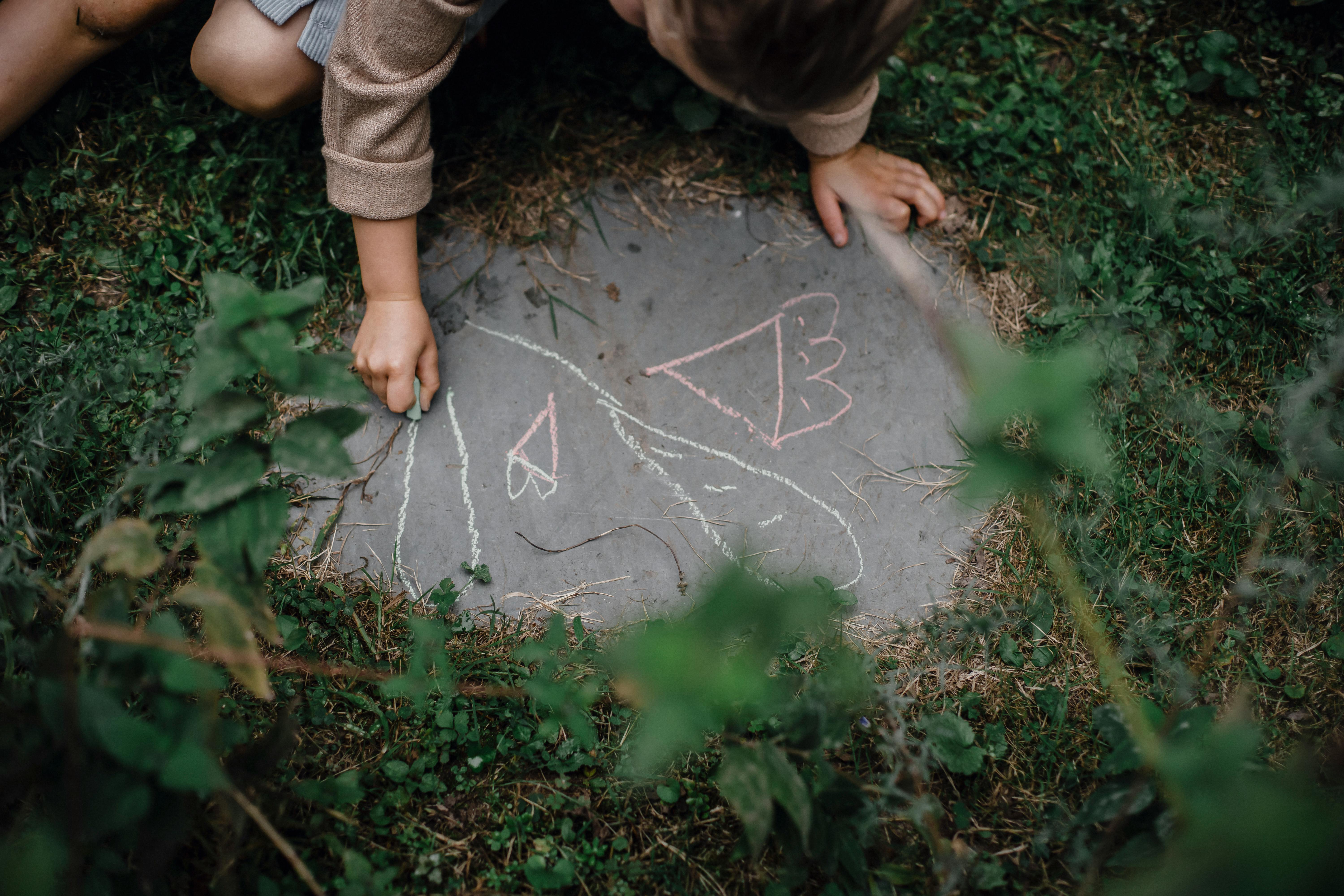child drawing picture on concrete block in grassy yard