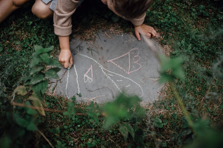 Child Drawing Picture On Concrete Block In Grassy Yard