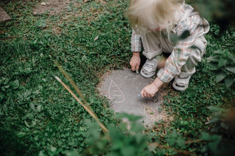 Little Boy Drawing Picture With Chalk In Garden