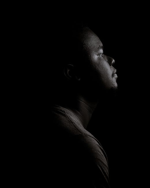 Moody black and white side profile portrait of a man in a studio with a dark background.