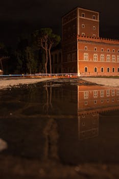 Captivating night view of Roman architecture reflecting in a street puddle.
