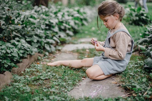 Cute stylish child playing with chalks in the garden t