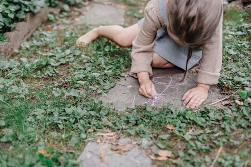 Free High angle of crop unrecognizable barefooted child painting on ground with colorful chalks while playing in green garden Stock Photo