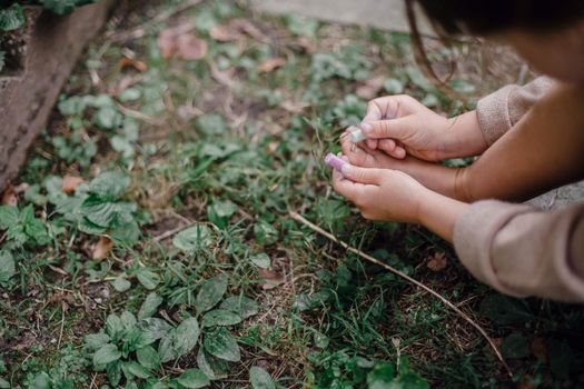 Unrecognizable child painting feet nails with chalks in garden