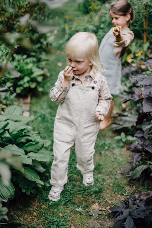 白とグレーの格子縞のボタンアップシャツと緑の植物の近くに立っている白いズボンの女の子