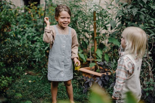 Cute little siblings playing together in garden near lush plants