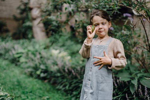 Funny kid holding ripe fruit in hand while resting in green garden
