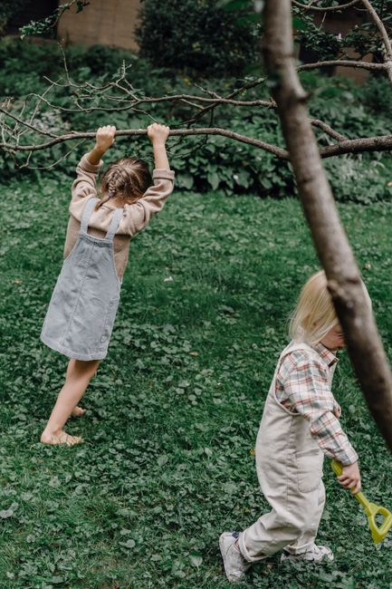 Full body of small adorable anonymous kids running and playing on lawn with fresh green grass and leafless tree