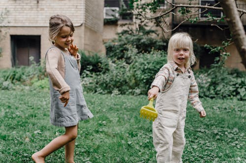 Cheerful cute boy and girl playing on green lawn in yard near buildings in summer