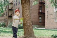 一个可爱有趣的男孩穿着休闲保暖的衣服，在院子里的树和建筑物附近玩着塑料耙子和铲子