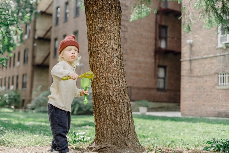 Little Cute Boy With Plastic Shovel And Rake Near Tree