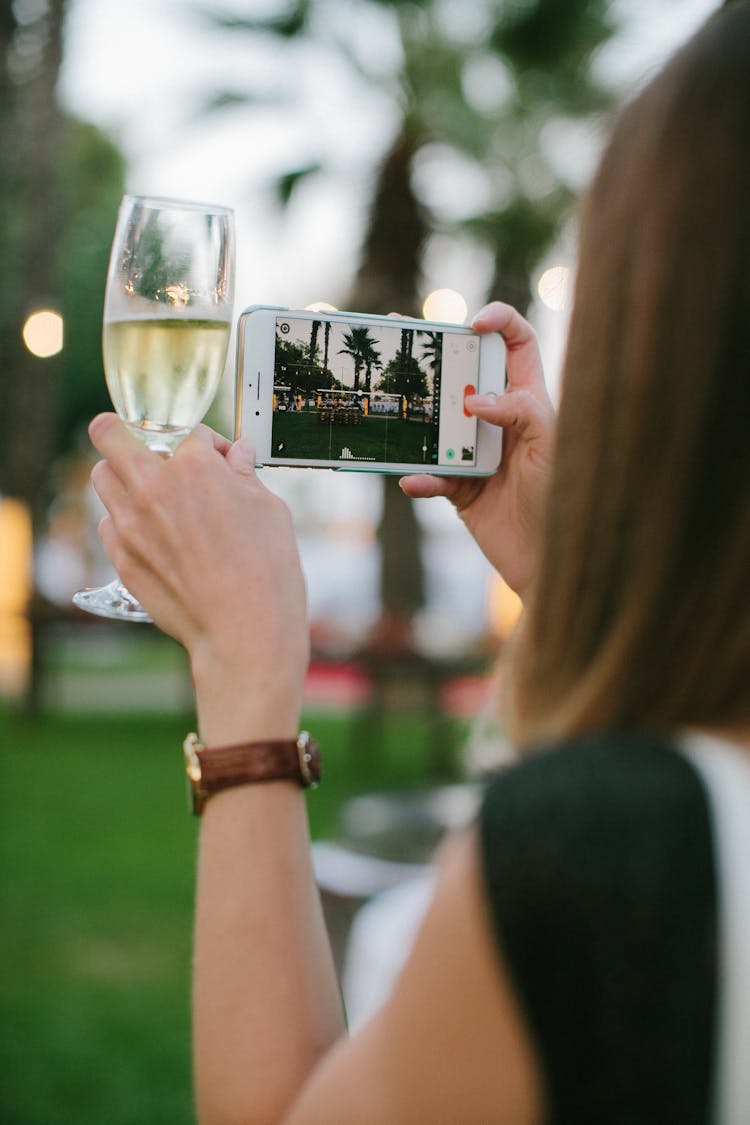 Woman Holding A Glass Of Wine And Taking Photo With Her Phone 