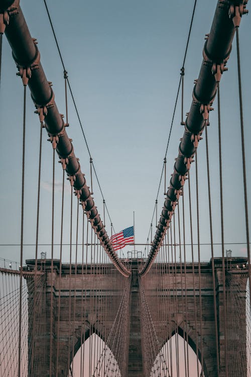 Top of famous suspension Brooklyn Bridge with American flag under cloudless blue sky