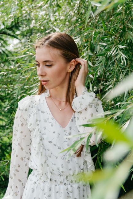 A serene portrait of a woman in a white floral dress amidst lush green leaves, exuding natural elegance.