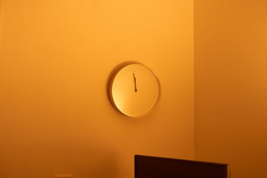 A minimalist wall clock in an orange-hued room with warm lighting, showcasing a simple design.