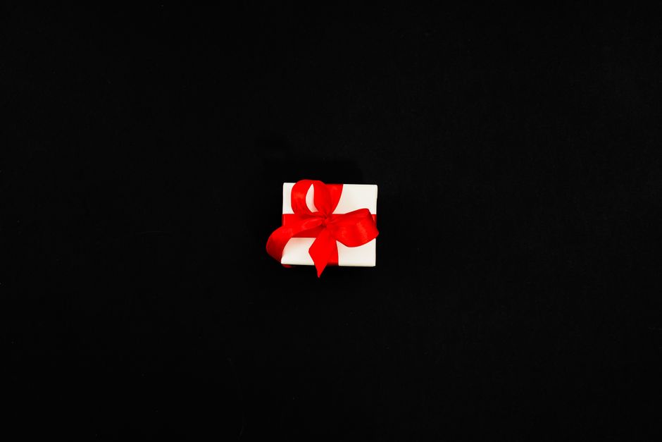 A white gift box tied with a red ribbon on a black background, perfect for celebrations.