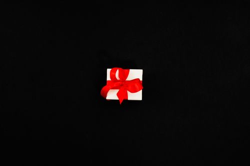 Free A white gift box tied with a red ribbon on a black background, perfect for celebrations. Stock Photo