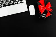 笔记本电脑平放在黑色星期五礼品盒旁，盒上系着红色蝴蝶结，非常适合在线购物主题