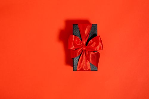 Free A stylish black gift box adorned with a luxurious red ribbon sits elegantly against a vivid red background. Stock Photo