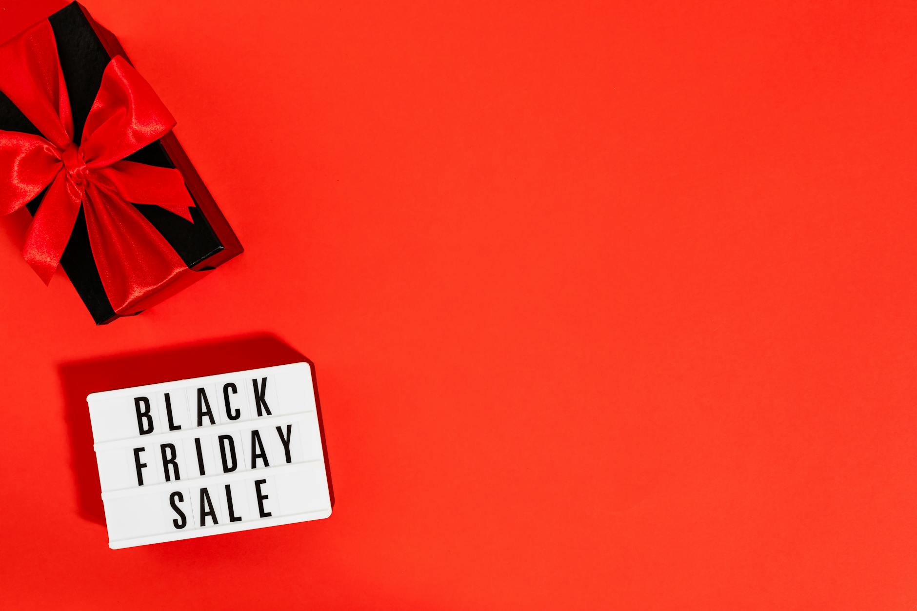 Stylish Black Friday sale display with a gift box on vibrant red background.
