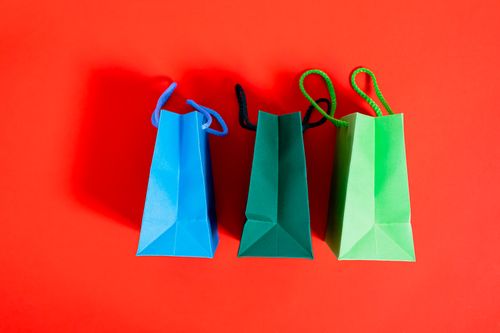 Free Three colorful paper shopping bags on a striking red backdrop, ideal for shopping and sale themes. Stock Photo