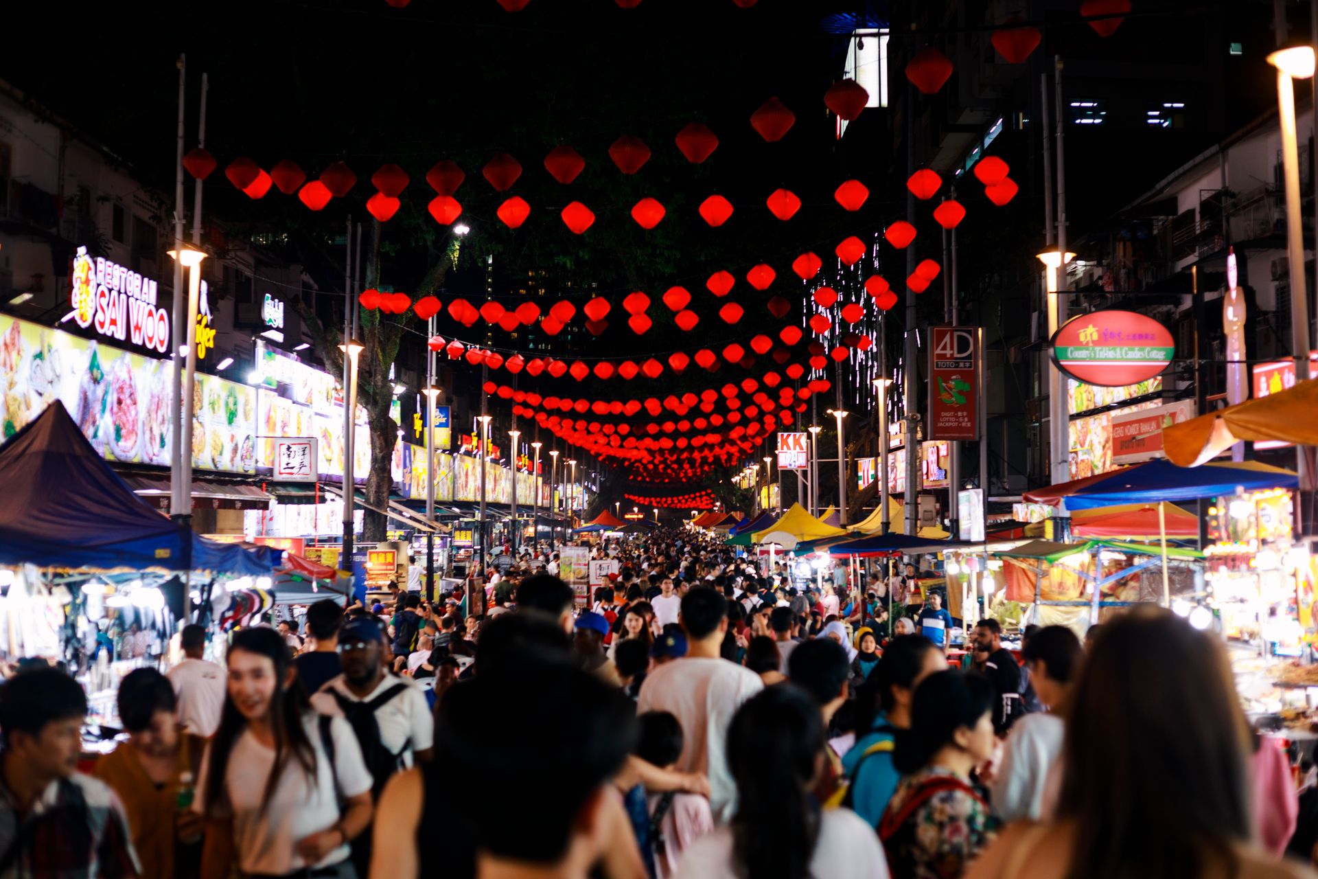 Bustling night market scene in Kuala Lumpur, featuring red lanterns and diverse crowd.