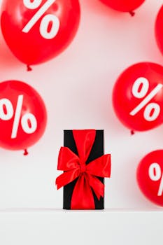 Black gift box with red ribbon surrounded by red balloons with percentage signs, ideal for sales promotions.