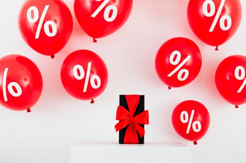 Free  A Gift With Red Ribbon in Between Red Balloons With Percentage Symbols on a White Background Stock Photo