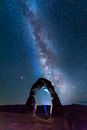 Person in Blue Jacket and White Pants Standing on Snow Covered Ground Under Starry Night