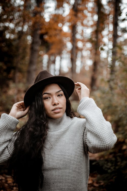 Positive ethnic woman touching hat brims in autumn park