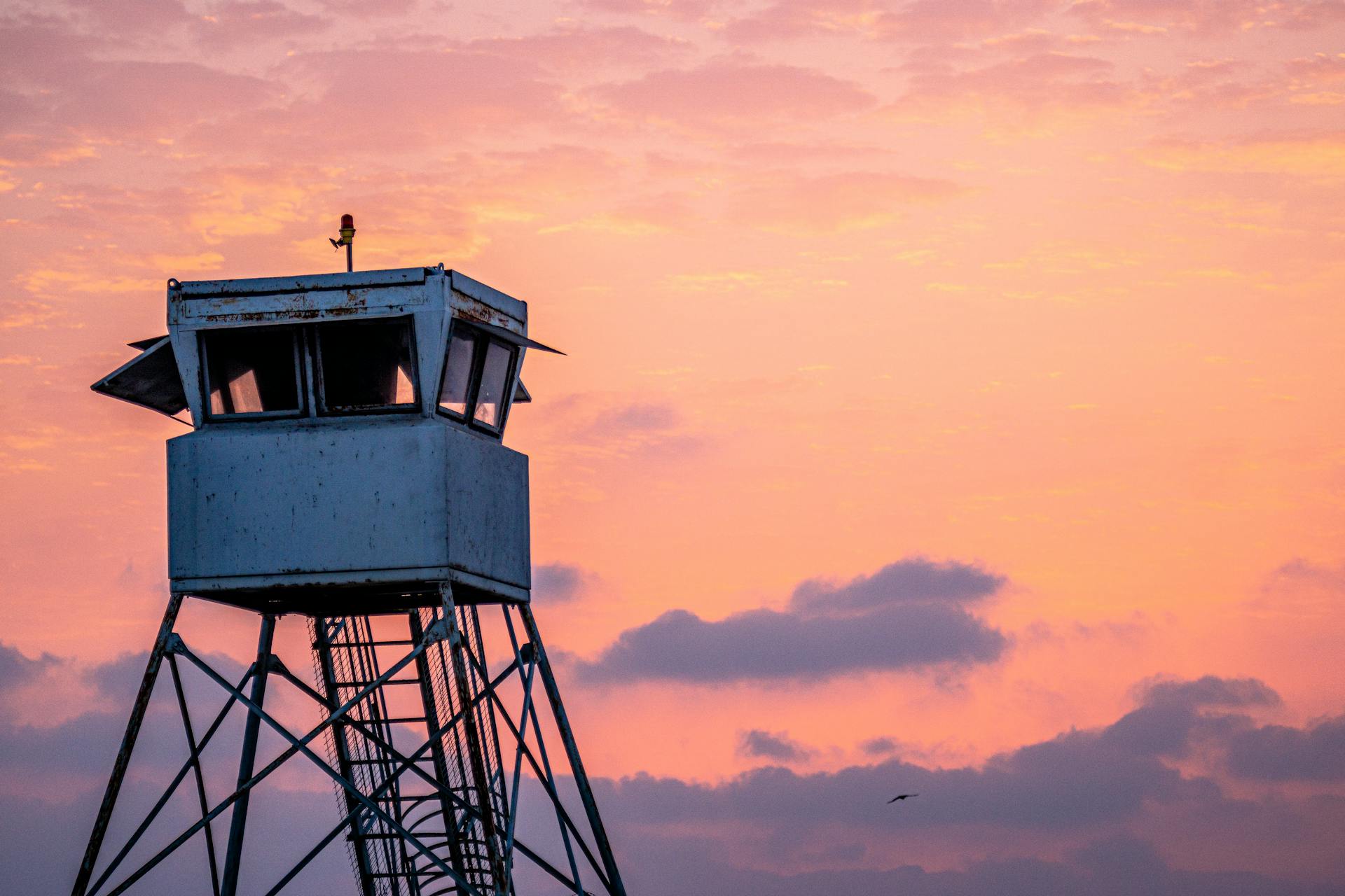 Silhouette of a lookout tower against a vibrant pink and orange sunset sky.