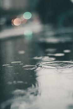 Rain drops dripping in puddle on street reflecting city lights on overcast day