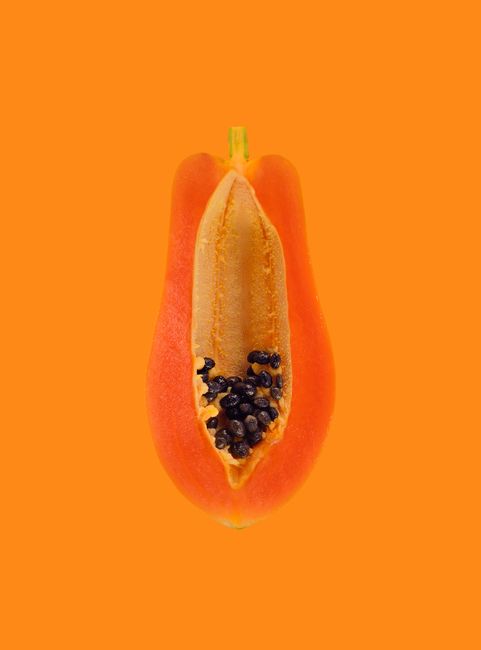 Close-up of a half-sliced papaya with seeds against a vibrant orange background.