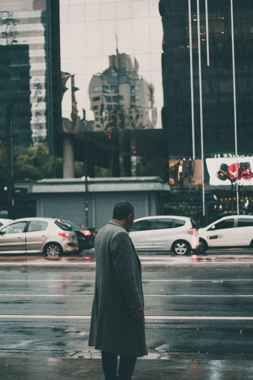 Free Urban scene with man in coat, cars, and building reflections on a rainy day. Stock Photo