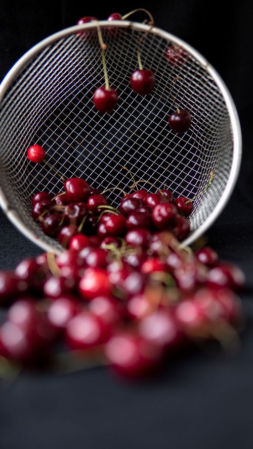 Free Round shaped metal strainer with pile of bright tasty cherries with shiny surface on black background Stock Photo
