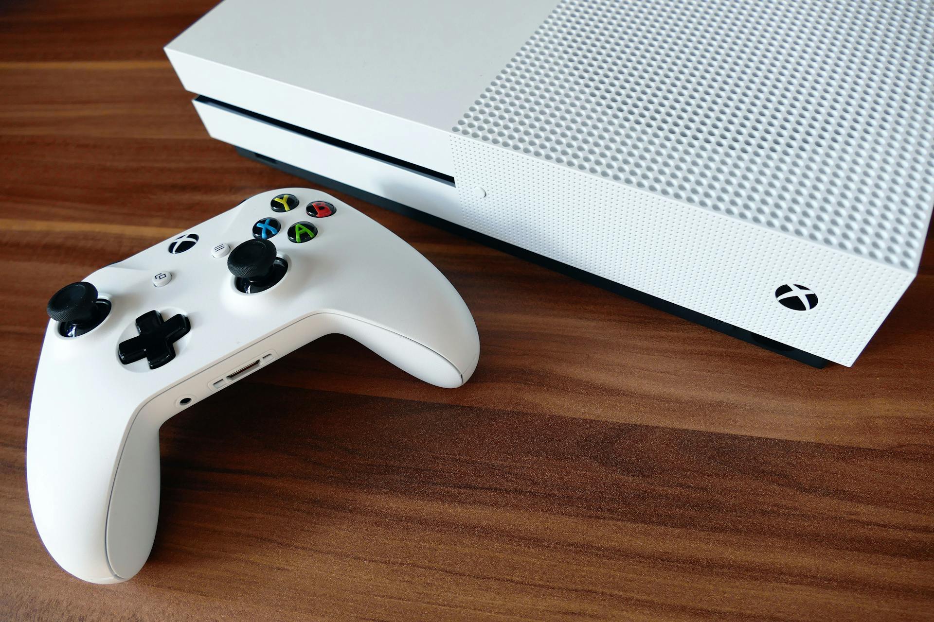 Close-up of a white Xbox console and controller on a wooden surface, ideal for gaming enthusiasts.