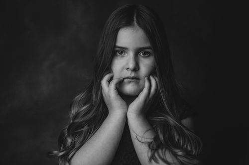 Free Black and white of cute little girl with long wavy hair touching cheeks and looking at camera against dark background Stock Photo