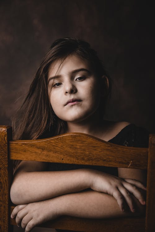 Free Pensive little child relaxing on chair in brown studio Stock Photo