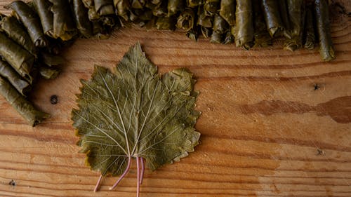 From above of vine leaf near pile of tasty sarma rolls on wooden cutting board