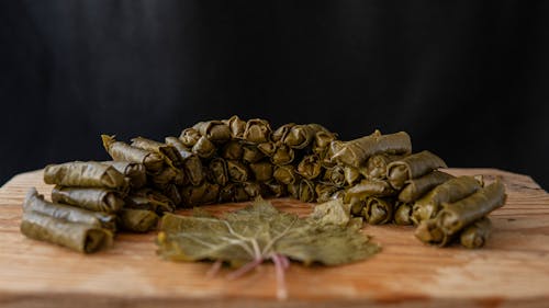 Delicious sarma rolls near vine leaf on wooden cutting board on black background