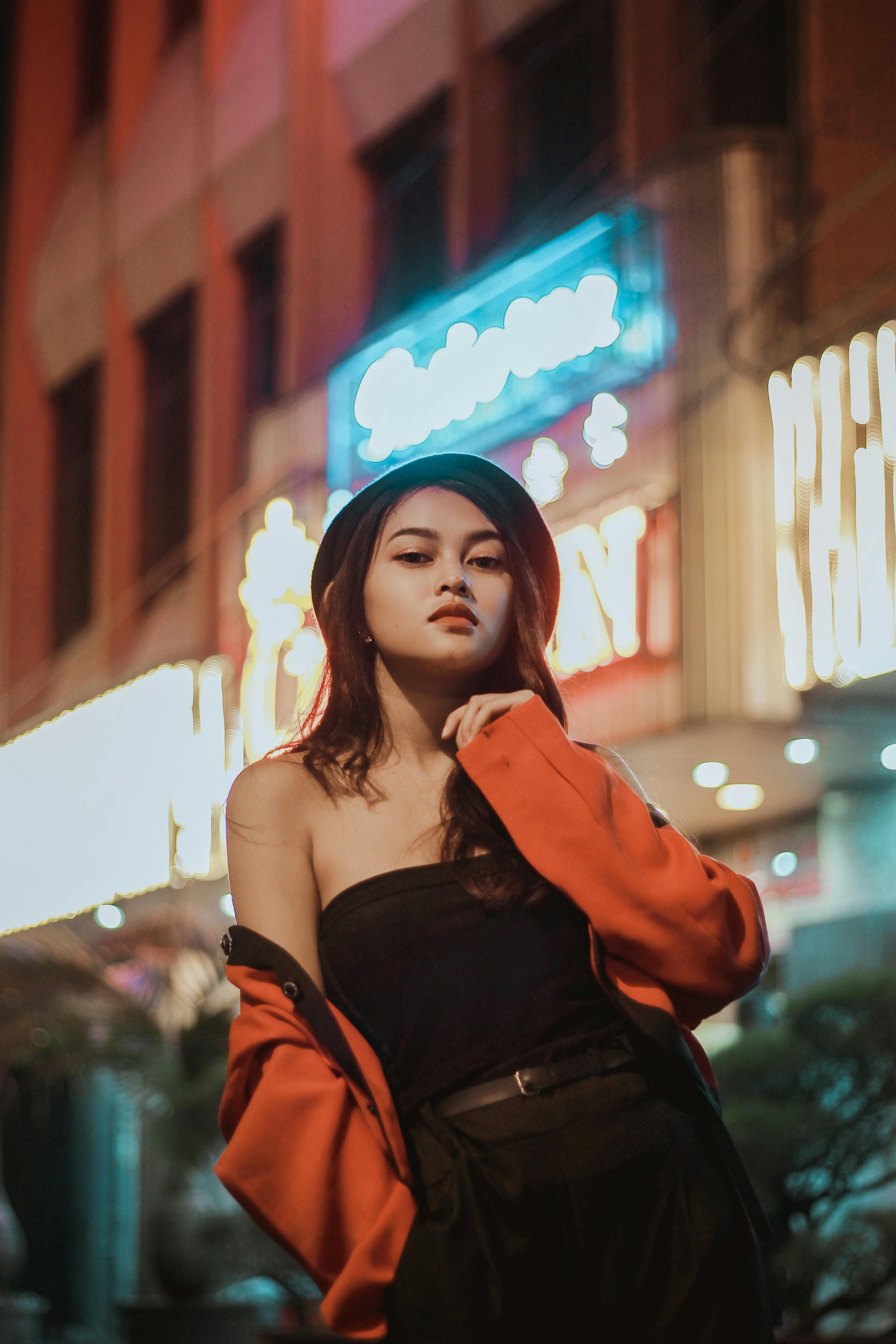 Confident woman in red jacket posing against vibrant neon signs at night in the city.