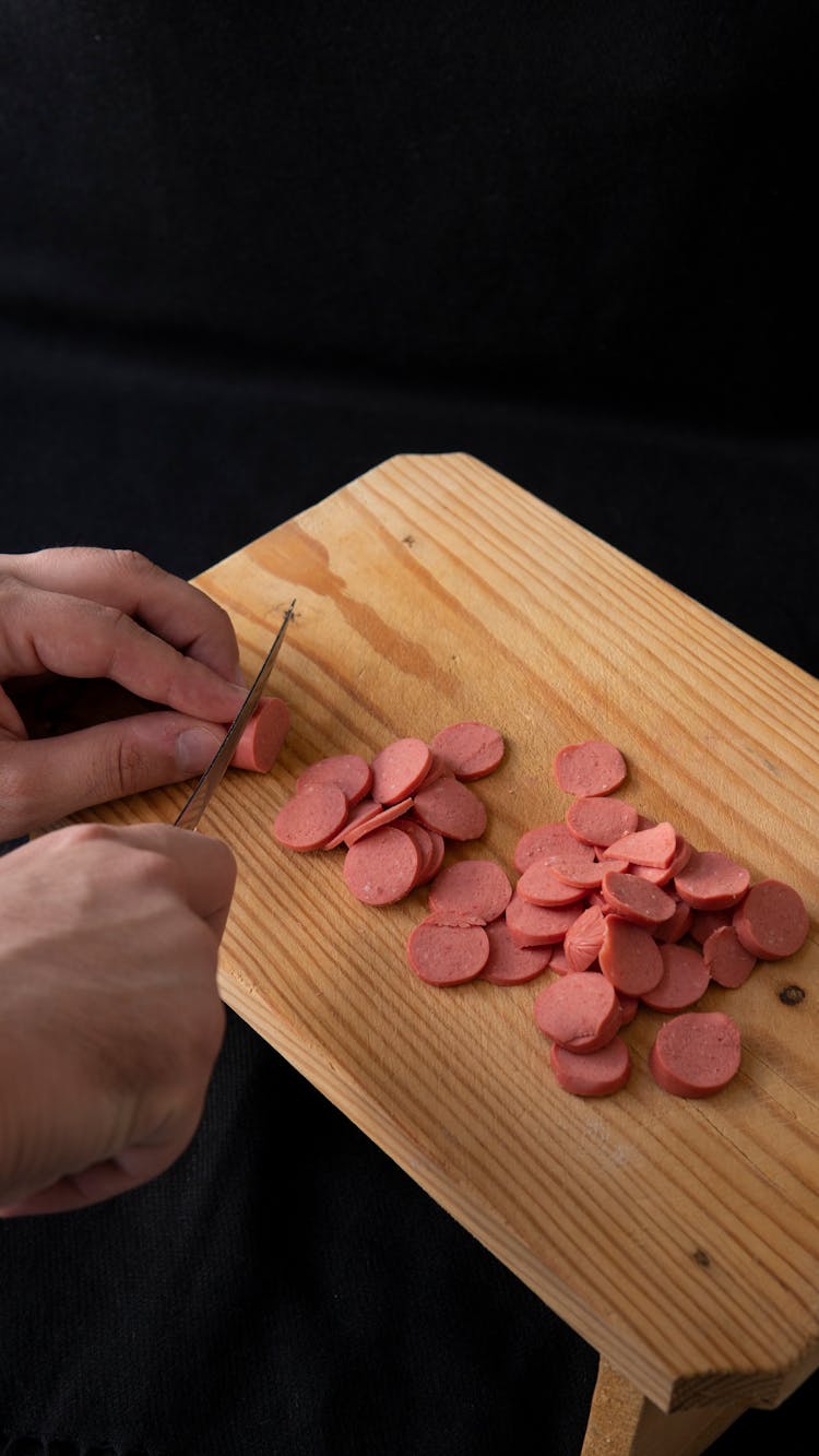 Crop Chef Cutting Sausage While Cooking In Kitchen